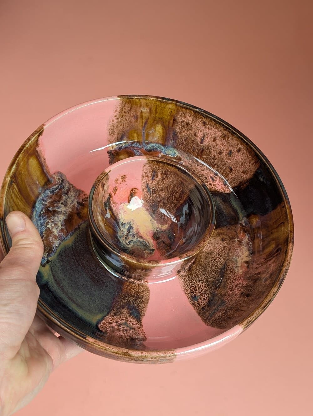 Hand met een roestbruin en roze geglazuurd schaaltje